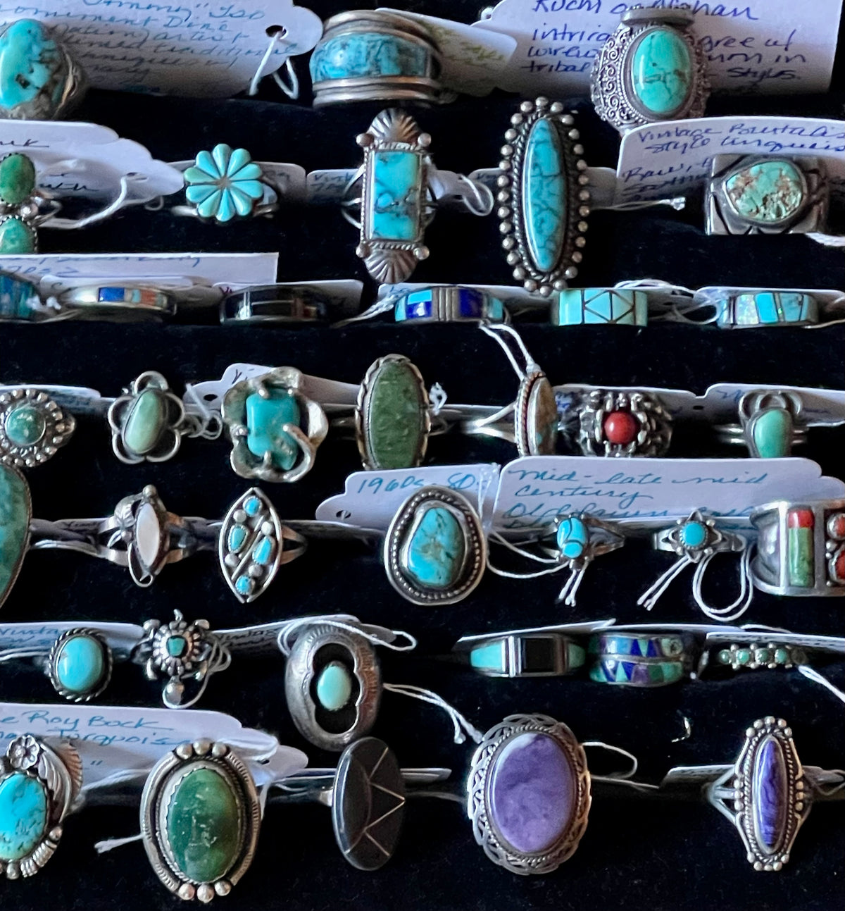 A close-up display of multiple silver rings featuring turquoise, green, purple, and red stones